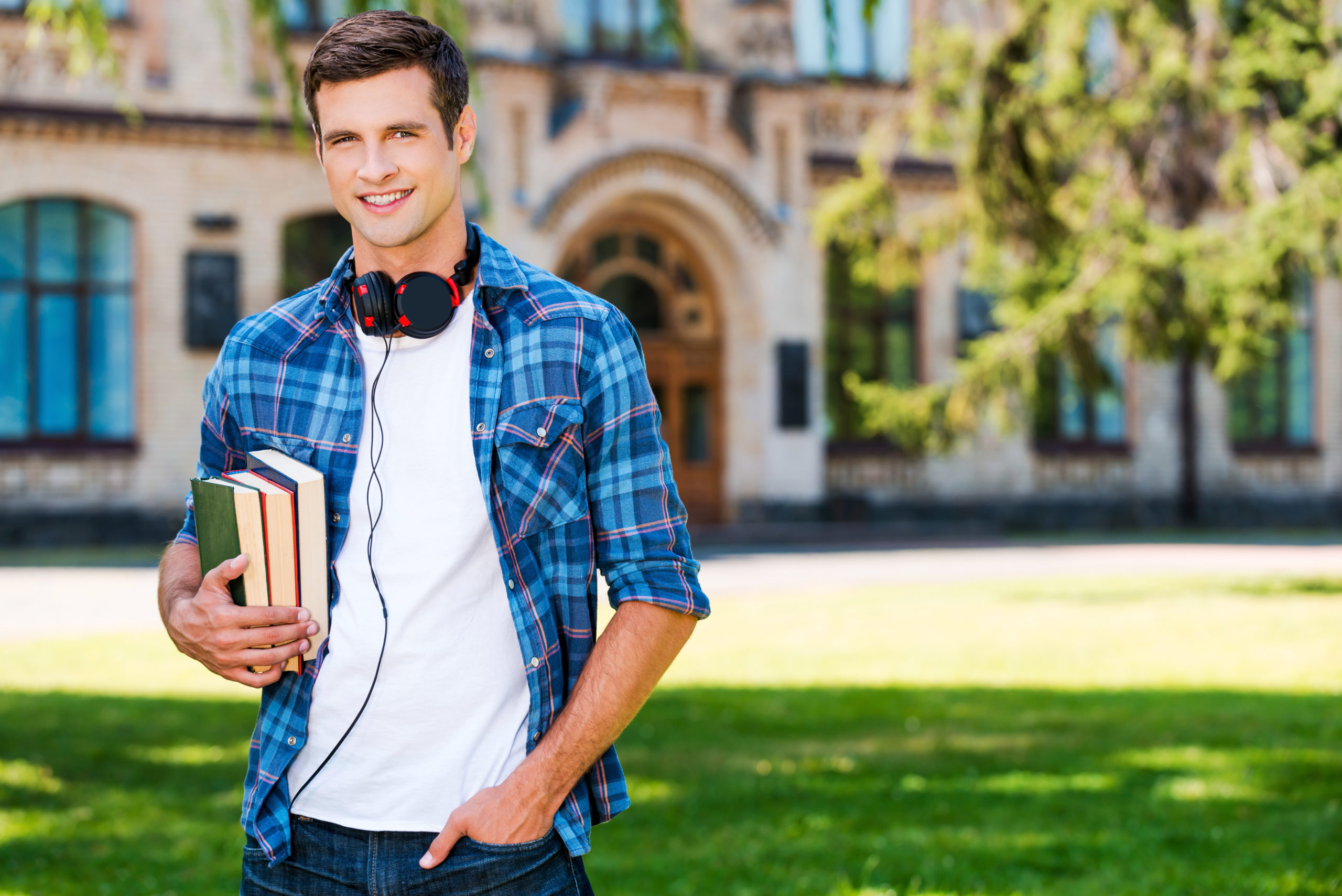Confident student. Handsome young man holding books and smiling while standing in front of his university